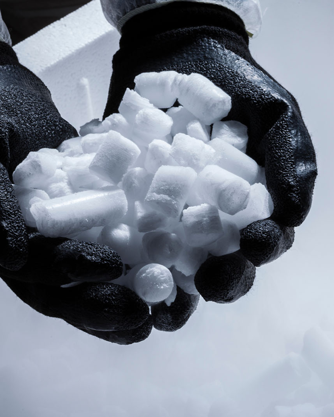 Black gloves holding a pile of white ice pellets against a white background